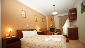 A hotel room with a large bed, two bedside tables with lamps, a wooden wardrobe, a small desk with a chair, and a fireplace. - Orama Hotel - Lake Plastira Fireplace Suite (Lake Plastiras)