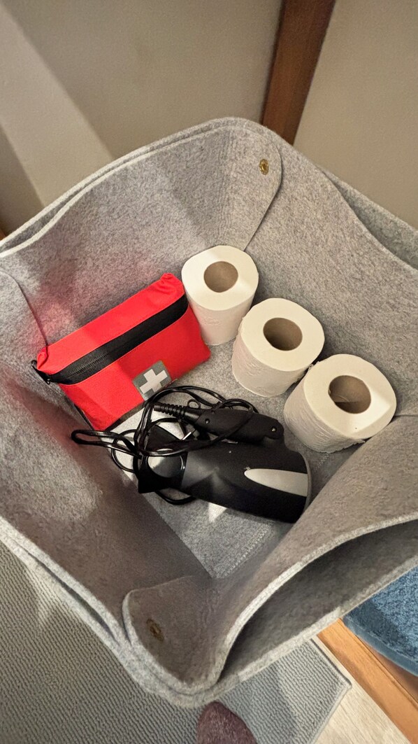 Un sac en feutre contenant une lampe de poche rouge et noire, deux rouleaux de papier toilette et une paire de gants noirs.