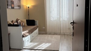 Ein Schlafzimmer mit Bett, Nachttisch, Lampe und einem Fenster mit durchsichtigen Vorhängen.