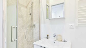 A modern bathroom with a glass shower enclosure, a white sink, and a mirror above the sink. - Charming Studio - 2P - Eiffel Tower (Paris)
