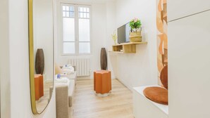 A modern hotel room with a large mirror, a television on a shelf, a potted plant, and a window with blinds. - Charming Studio - 2P - Eiffel Tower (Paris)