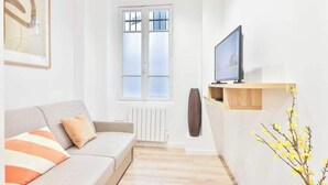 A modern living room with a sofa, a television, a radiator, and a window. - Charming Studio - 2P - Eiffel Tower (Paris)