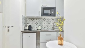 A compact kitchen with white cabinets, a microwave, a small refrigerator, and a white round table with a vase of yellow flowers. - Charming Studio - 2P - Eiffel Tower (Paris)