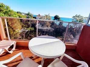 A balcony with a round table and white chairs, overlooking a coastal area with trees and buildings. - Studio for 4 with Wi-Fi and terrace (Roquebrune-Cap-Martin)