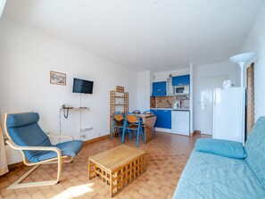 A compact living space with a kitchenette, a dining area with blue chairs, a sofa, and a television mounted on the wall. - Apartment for 6, 2 bedrooms with Wi-Fi in Roquebrune-Cap-Martin (Roquebrune-Cap-Martin)