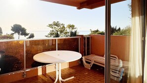A balcony with a round table and chairs, overlooking a body of water and trees. - Apartment 6 people, sea view, unlimited Wi-Fi (Roquebrune-Cap-Martin)