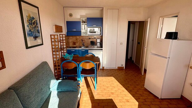 Ein gemütlicher Wohnbereich mit einer Couch, einem Esstisch mit Stühlen, einer Küchenzeile und einem Kühlschrank.