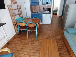 Un espai vital compacte amb una cuineta, una zona de menjador amb taula i cadires, i un petit sofà.