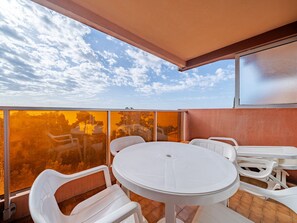 Ein Balkon mit rundem Tisch und weißen Stühlen, großen Fenstern und Blick zum Himmel.