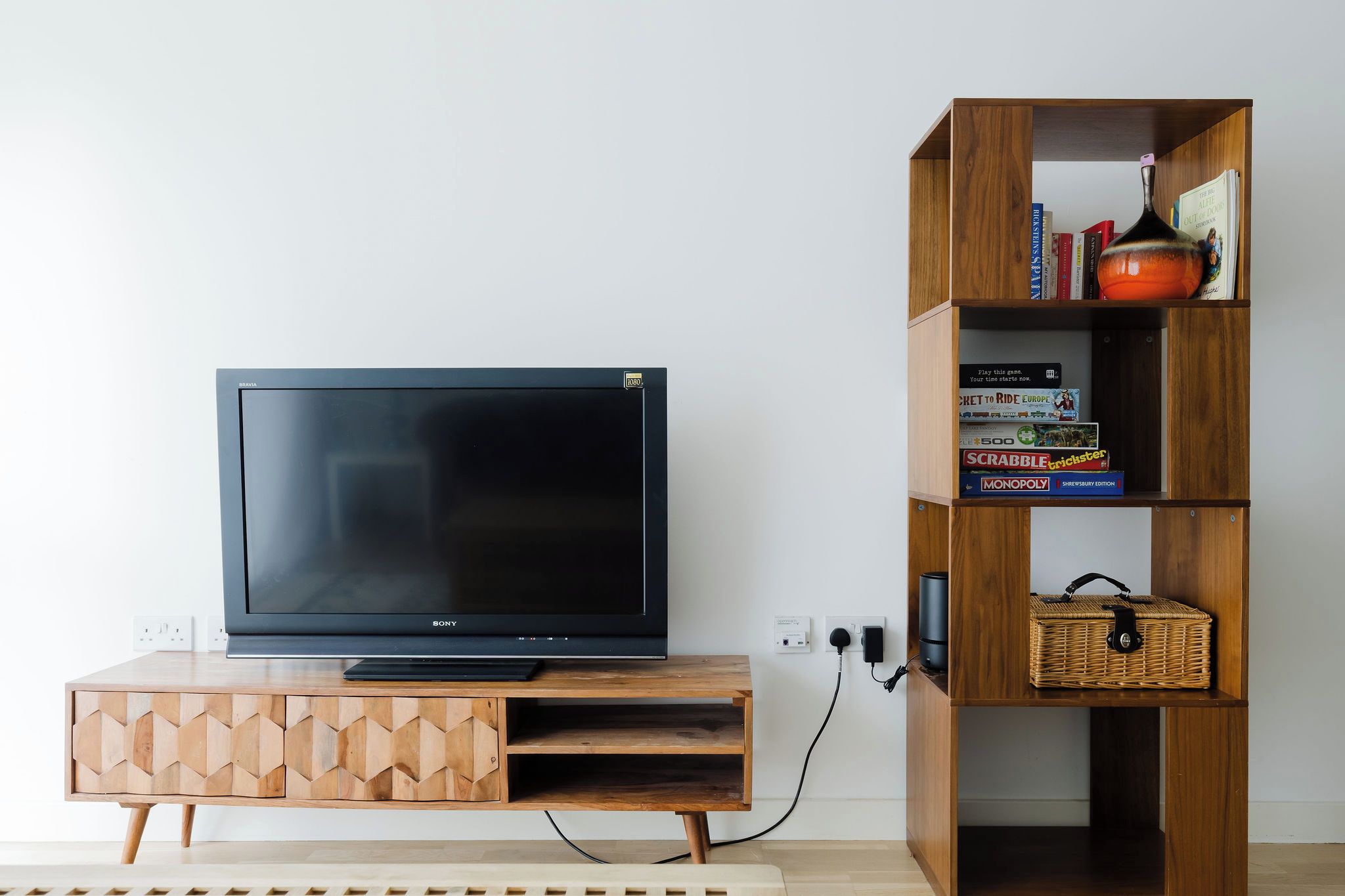 A flat-screen TV on a wooden stand with a bookshelf beside it.