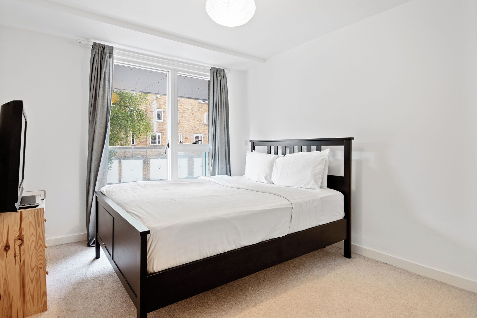 A bedroom with a bed, a wooden nightstand, and a window with curtains.