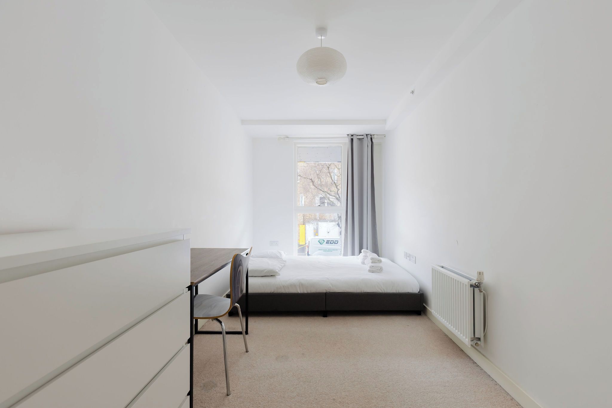 A small, bright room with a bed, a desk, and a chair.