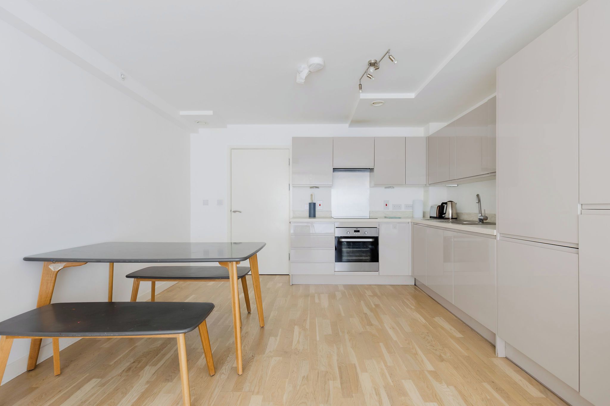 A modern kitchen with white cabinets, a built-in oven, and a dining area with a table and chairs.