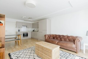 A modern living space with a kitchen, a leather sofa, and a dining area. - Calming 2BDR Hideaway 25 Mins From Tower Bridge (Greater London)