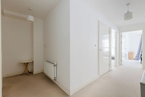 A hallway with white walls, a radiator, a small table, and a door leading to another room. - Calming 2BDR Hideaway 25 Mins From Tower Bridge (Greater London)