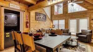 A wooden cabin interior with a dining table set for four, a fireplace, and a kitchen area with a stove. - Close to Gatlinburg, 3 bedroom, 2 bath, hot tub, pool table (Gatlinburg)