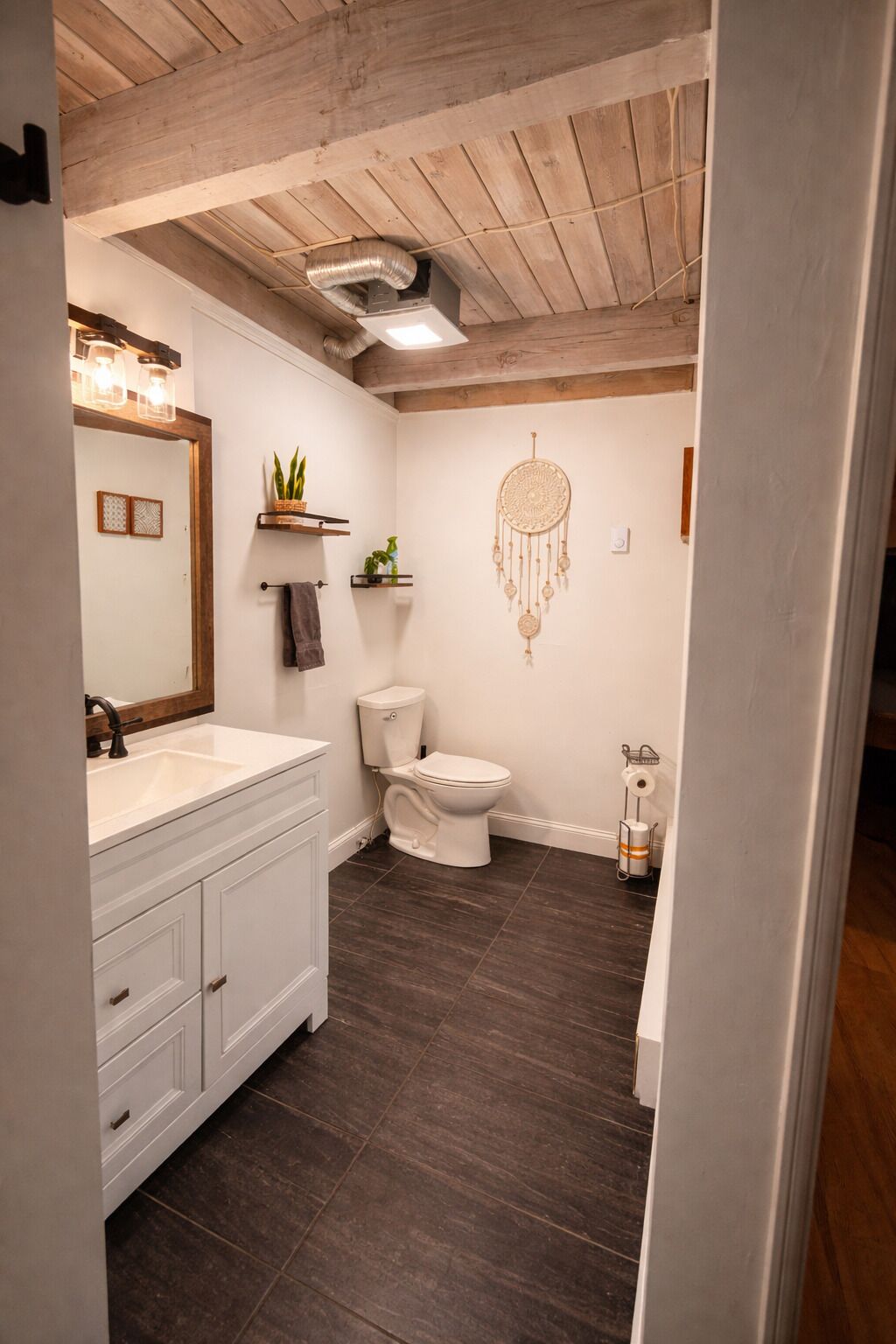 Une salle de bain avec un meuble-lavabo blanc, des toilettes et un attrape-rêves accroché au mur.
