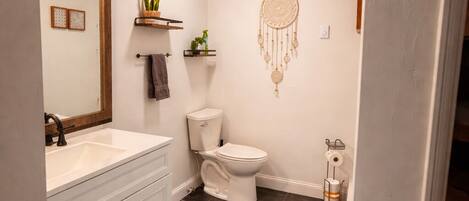 Une salle de bain avec un meuble-lavabo blanc, des toilettes et un attrape-rêves accroché au mur.