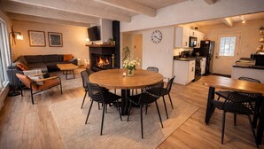 En moderne stue med pejs, et spiseområde med et rundt bord, og et køkken med hvide skabe.
