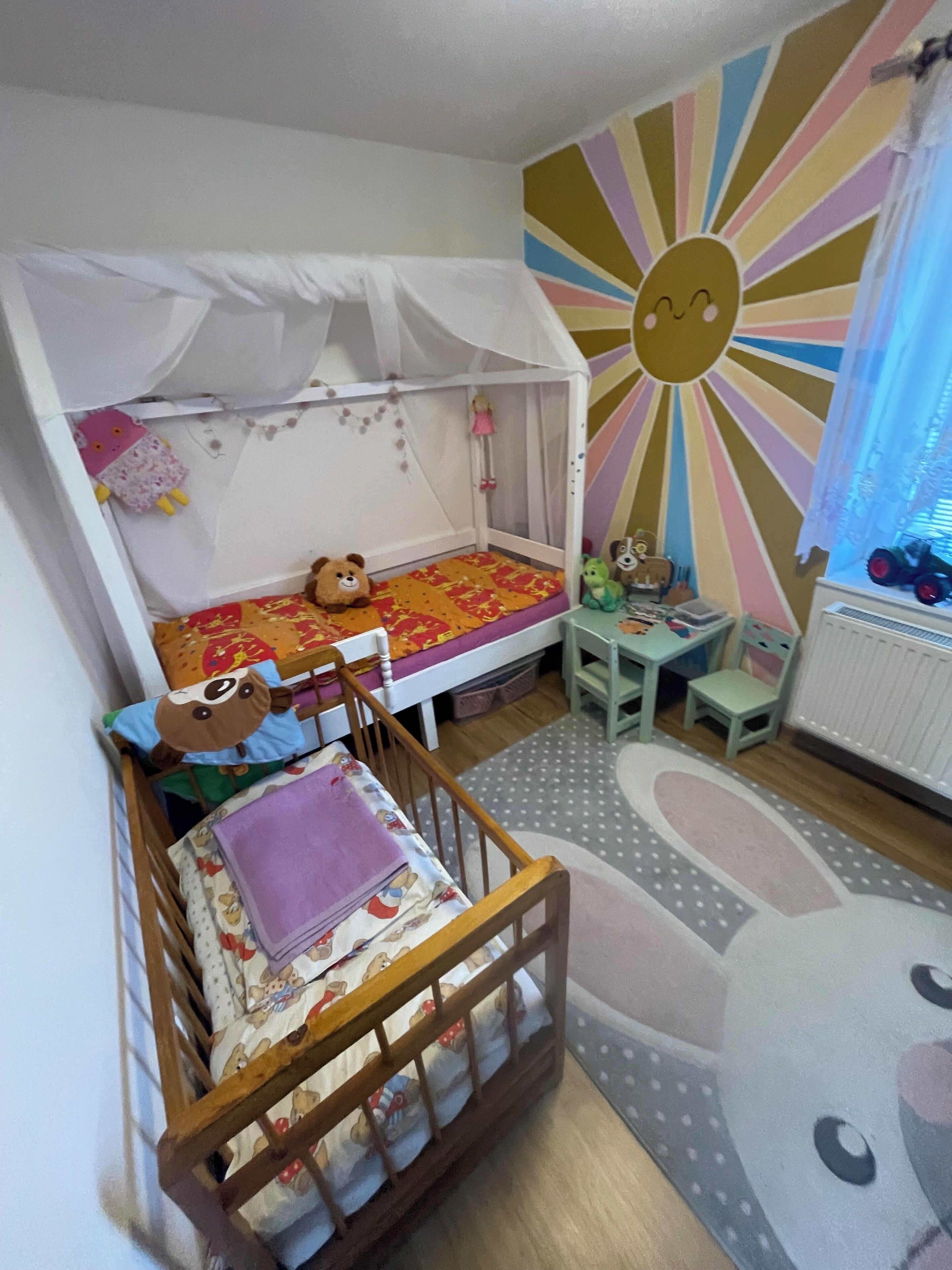 A child's bedroom with bunk beds, a play area, and a sun-themed wall.