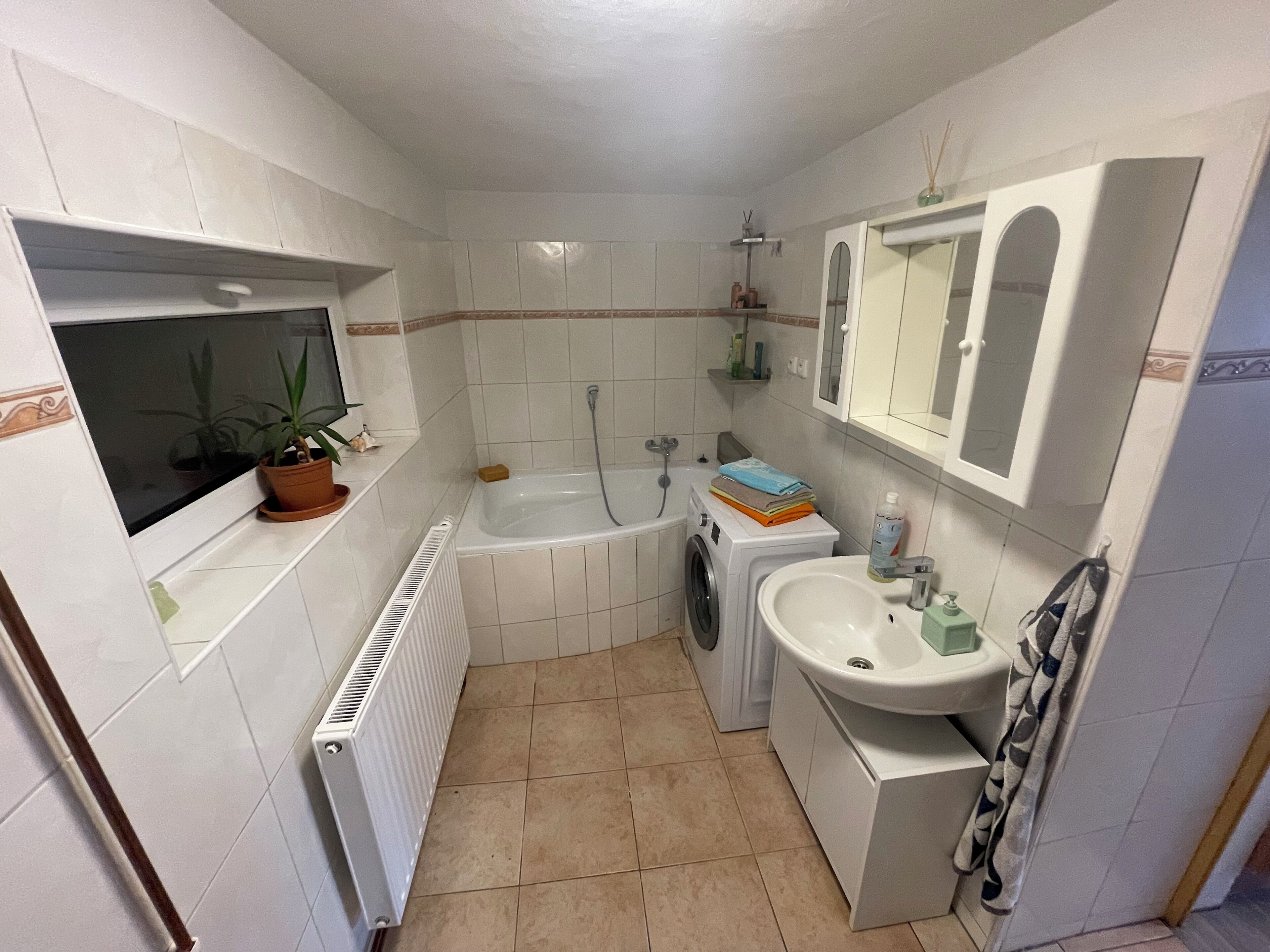 Un bany compacte amb banyera, rentadora, un lavabo i un mirall.
