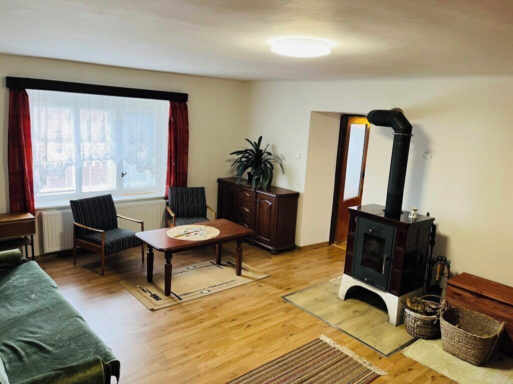 A cozy living room with a wooden floor, a green sofa, a dining table with chairs, a fireplace, and a window with curtains.