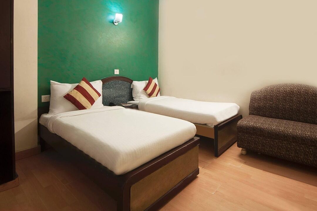 A room with two single beds, a sofa, and a green accent wall.