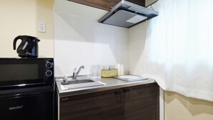 Una kitchenette compacta con microondas, hervidor, pileta y placares.