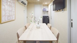 Un comedor moderno con una mesa larga, sillas, un florero con flores y un televisor en la pared.
