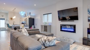 Una sala de estar moderna con un sofá seccional, un televisor de pantalla plana, una chimenea y una cocina al fondo.