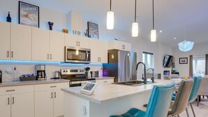 Una cocina moderna con una isla central, electrodomésticos de acero inoxidable y taburetes de bar azules.