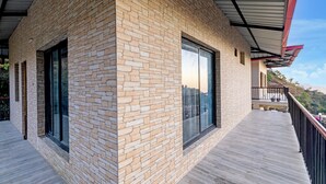 A modern building with a stone facade, large windows, and a wooden deck. - Alaya Stays Vyasa Duplex With Views (Mussoorie)