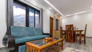 A living room with a sofa, a glass coffee table, wooden chairs, and a view of a mountainous landscape through large windows. - Alaya Stays Vyasa Duplex With Views (Mussoorie)