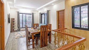 A dining area with a wooden table and chairs, a TV mounted on the wall, and a staircase with ornate railings. - Alaya Stays Vyasa Duplex With Views (Mussoorie)
