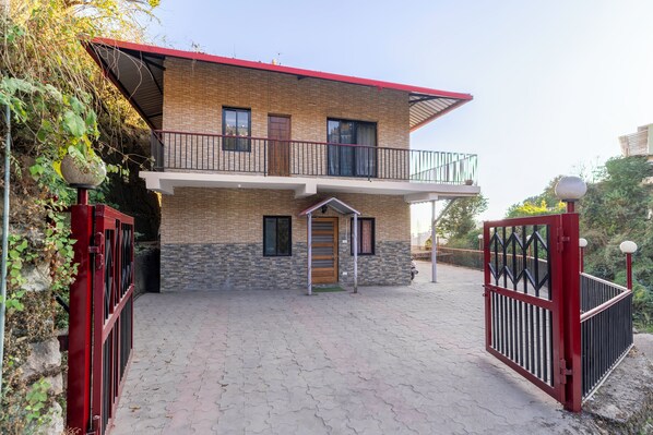 A two-story house with a balcony, a gated entrance, and a paved driveway.