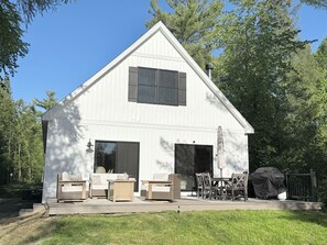 A white building with a gabled roof, large windows, and a covered patio area with outdoor furniture. - Driftwood on Torch River (Rapid City)