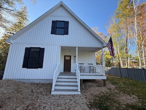 A white two-story house with a front porch, a wooden staircase, and an American flag. - Driftwood on Torch River (Rapid City)