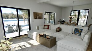 Uma sala de estar ampla com um sofá branco, uma mesa de centro e uma grande janela com vista para uma área externa coberta de neve.