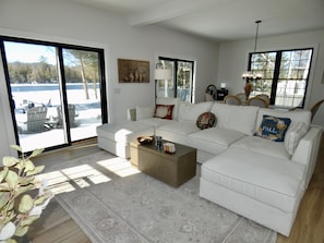 A spacious living room with a white sofa, a coffee table, and a large window offering a view of a snowy outdoor area. - Driftwood on Torch River (Rapid City)