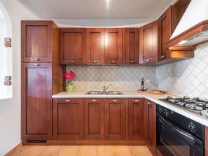 A kitchen with wooden cabinets, a stainless steel sink, and a gas stove. - Home Thoughtfully Designed for the Comfort (Siniscola)
