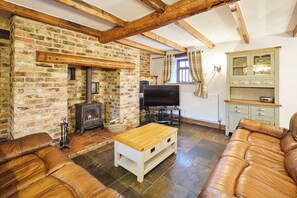 A cozy living room with exposed wooden beams, a brick fireplace, a television, and leather sofas. - Host Stay The Stable Bridlington (Bridlington)