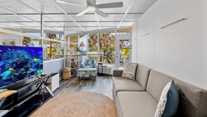 A spacious living room with a large TV, a sofa, and a ceiling fan. - Ocean Oasis - Ocean View At Symphony Beach Club and King Bed (Ormond Beach)
