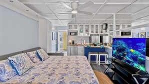 A modern hotel room with a large bed, a kitchenette, a dining area, and a TV displaying an underwater scene. - Ocean Oasis - Ocean View At Symphony Beach Club and King Bed (Ormond Beach)