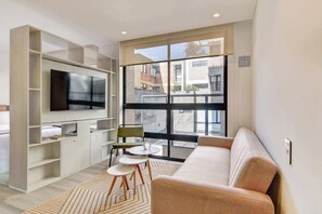 A modern living room with a flat-screen TV, a sofa, a dining table with chairs, and a large window offering a view of buildings. - w Stylish Radiant Loft in Chapinero (Bogotá)