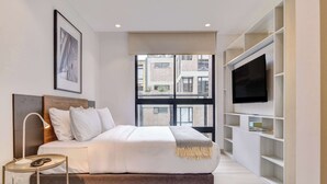A modern bedroom with a bed, bedside table, TV, and a window with a city view. - w Stylish Radiant Loft in Chapinero (Bogotá)