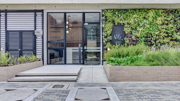 A modern building entrance with a glass door, a brick planter with greenery, and a metal shutter to the left. - w Stylish Radiant Loft in Chapinero (Bogotá)