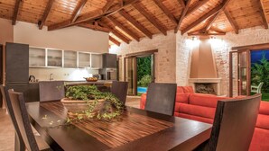 Eine moderne Küche mit eingebauten Geräten, ein Essbereich mit Holztisch und -stühlen sowie ein rotes Sofa in einem Wohnzimmer mit Steinwänden.