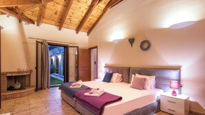 Ein Schlafzimmer mit einem großen Bett, einem Nachttisch, einem Kamin und Blick ins Freie.