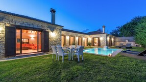 Ein Steinhaus mit Pool, Sitzgelegenheiten im Freien und einem gut beleuchteten Innenraum.