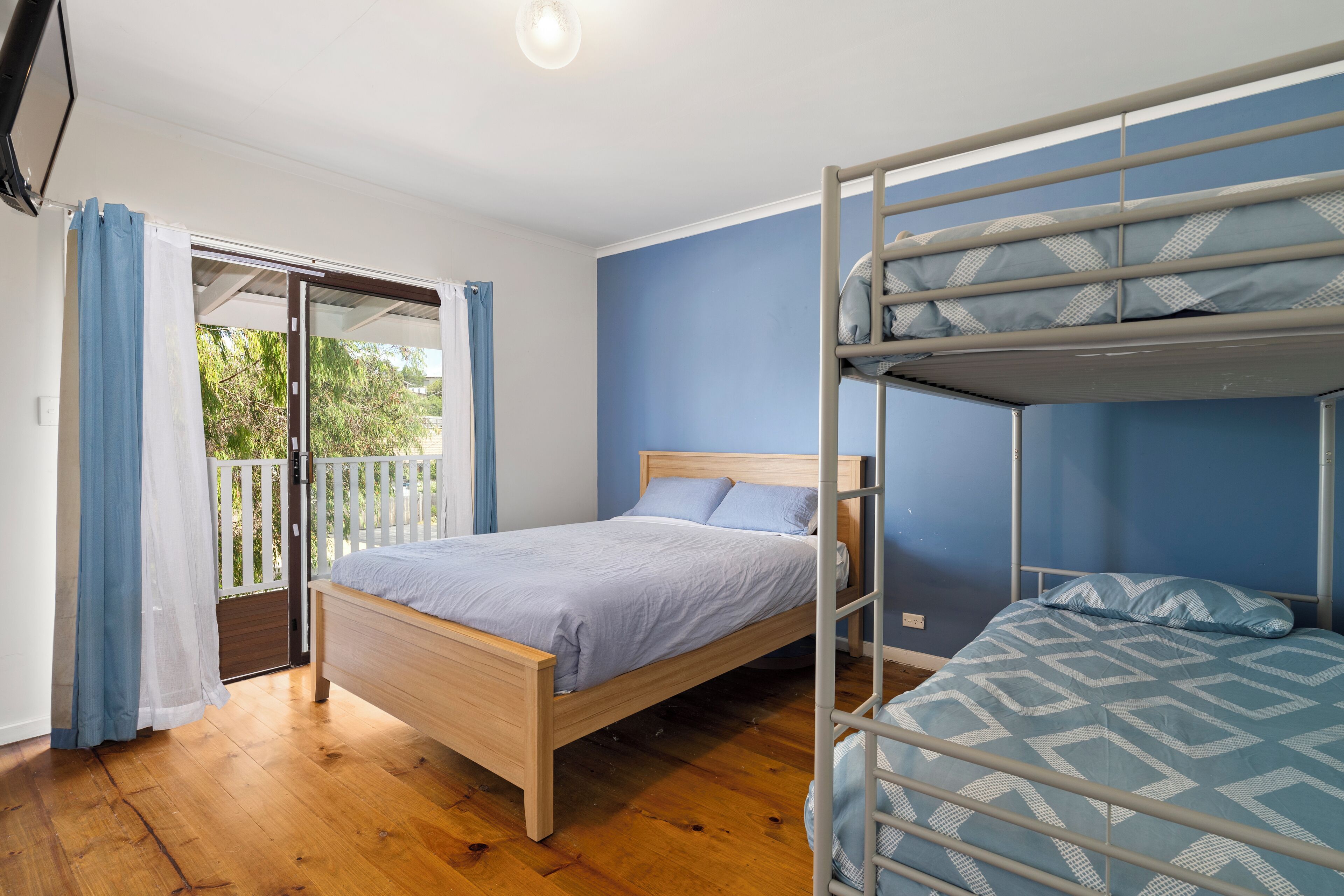 Un dormitorio con una cama de madera, una cama nido y un ventanal corredero que da a un espacio exterior.